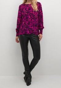 Magenta og sort langærmet top med blomstermønster, parret med tætsiddende sorte læderbukser og spidse sorte hæle.