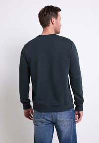 Felpa grigia scura con maniche lunghe, polsini a costine e scollatura a girocollo. Abbinata a jeans blu chiaro, con vestibilità classica e tasche posteriori.