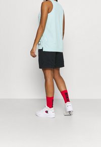 Ljusblå utan ärmar nättröja, svarta shorts och röda strumpor med svart text. Har vita sportskor med logotyp.