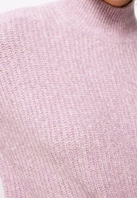 Nahaufnahme eines weichen, rosa gestrickten Rollkragensweaters mit einem sichtbaren strukturierten Stichmuster auf dem Stoff.