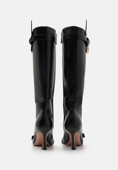 Botas de cuero negras hasta la rodilla con tacones delgados, cremalleras laterales y una correa en el tobillo. Textura suave con un diseño limpio y minimalista.