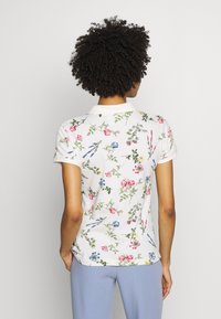 Weißes Poloshirt mit floralem Print in Pink, Blau und Grün. Mit Kragen, kurzen Ärmeln und einer taillierten Silhouette.