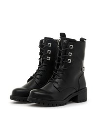 Botas de tobillo de cuero negro con suela robusta, cordones y acentos metálicos decorativos en forma de cuadrado en los lados. Presentan un cierre con cremallera.