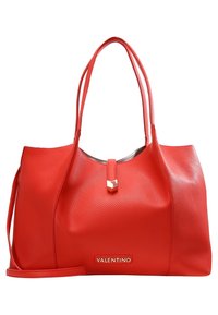 Punainen nahkainen kestokassi, jossa on teksturoitu pinta, kaksi kahvaa, kultaiset yksityiskohdat ja logo edessä. Sisältää irrotettavan hihnan.