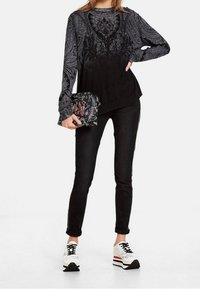 Schwarz-graues Langarmoberteil mit Paisleymuster, kombiniert mit schwarzen engen Jeans und weißen Sneakern mit schwarzen und roten Akzenten.