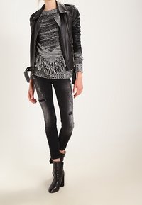 Kobieta ubrana w czarną skórzaną kurtkę, szary sweter z frędzlami, podarte czarne jeansy skinny oraz czarne botki na obcasie.