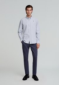 Hellblau-weiß gestreiftes Button-Down-Hemd, lange Ärmel, eine Tasche auf der linken Brust, kombiniert mit dunklen Hosen und schwarzen Schuhen.