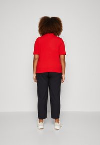 Röd kortärmad polo skjorta, mörka byxor och vita sneakers. Tyget verkar slätt, med en enkel design och standard passform.