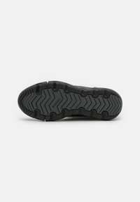 Suela de zapato de goma negra con un patrón de relieve en zigzag, con el nombre de la marca "SOREL" cerca de la zona del talón.