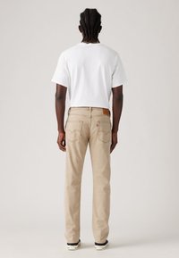 Beige denim jeans met achterzakken, bruin leren label, normale pasvorm, gecombineerd met een eenvoudig wit T-shirt en zwarte schoenen.