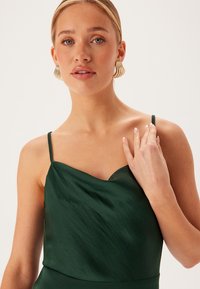 Zelené saténové šaty s výstřihem do V a tenkými ramínky. Tkanina má mírný lesk a jemně se splétá. Vyznačují se svou hladkou texturou.