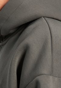 Grå bomulds hoodie med struktureret stof, en stor hætte og en afslappet pasform, med synlige sømme og glatte sømme.