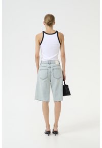 Ljusblå denimshorts med slitna kanter, matchade med en vit linne med svart kant. Modellen håller en liten svart handväska.