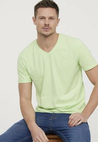 T-shirt vert néon à manches courtes et col en V, fabriqué en mélange de coton doux, avec un petit logo en relief sur la poitrine. Assorti à un jean bleu.