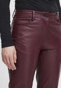 Burgundy fake læderbukser med slim fit, der har knaplukning, sidelommer og syninger langs sømmene.