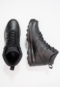 Crne kožne planinarske čizme s visokim gornjim dijelom, vezanjem, čvrstim potplatom i podstavljenim ovratnikom. Nike logo na strani.
