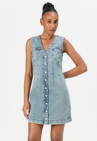 Jeanskjole med V-hals, uten ermer, lys blå farge, frontknapplukking og to vertikale sømdetaljer.