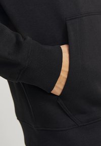Felpa nera con cappuccio caratterizzata da polsini a coste, una tasca frontale e una texture del tessuto liscia. Il design è semplice e funzionale.