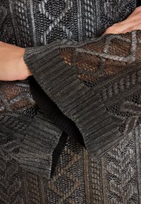 Dunkelgrauer Strickpullover mit komplexen geometrischen Mustern. Verfügt über einen gerippten Kragen und offene Strickdetails an den Ärmeln. Schimmernde Textur in Grautönen.