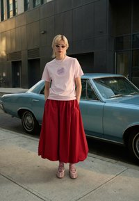 Rosa bomullst-shirt med tryck, röd volangkjol och blekrosa snörskor. Bakgrunden visar en ljusblå vintagebil.