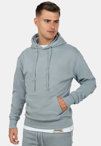 Felpa grigia chiara realizzata in morbido tessuto, con tasca a marsupio, cappuccio regolabile con lacci e branding discreto sul petto e sulla manica.