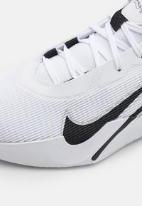 Nike-Schuh mit strukturiertem weißem Obermaterial, schwarzen Akzenten und einem markanten schwarzen Swoosh-Logo. Verfügt über weiße Schnürsenkel und ein schlankes, modernes Design.