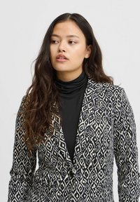 Mustvalge mustriga bleiser, mis on slim fit lõikega, varustatud noth-lapeli, ühe nupuga kinnituse ja kahe esikotiga.