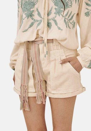 Bermudas de color beige claro con una textura suave, que presentan bolsillos laterales y un cinturón trenzado multicolor con borlas. Blusa con bordado floral.