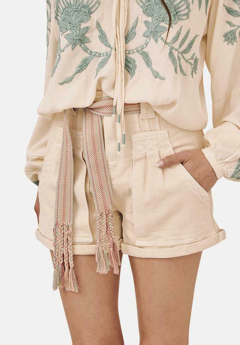 Bermudas de color beige claro con una textura suave, que presentan bolsillos laterales y un cinturón trenzado multicolor con borlas. Blusa con bordado floral.