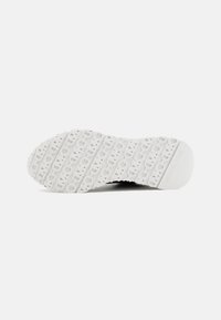 Semelle de chaussure blanche avec motif découpé répétitif et "MICHAEL KORS" embossé au niveau du talon sur un fond blanc uni.