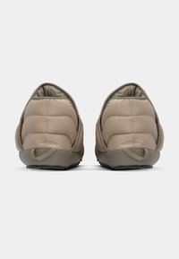 Chaussons beiges matelassés avec un dos arrondi, une tige texturée et une semelle en caoutchouc dotée d'un tirant pour un enfilage facile. Doublure intérieure douce.