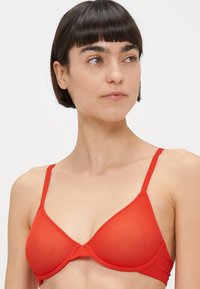 Piros merevítős melltartó sima textúrával, háromszög alakú kosarakkal és állítható vékony pántokkal. Klasszikus dizájn minimális részletezéssel.