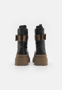Zwarte leren veterschoenen met een stevige bruine rubberen zool, voorzien van een zijband met het "PINKO" logo in vetgedrukte letters.