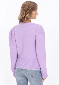 Lavendelfarbenes Sweatshirt mit geripptem Saum, gepufften Ärmeln und offenen Maschen am Bund. Das Material wirkt weich und gestrickt.