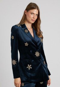 Blazer de terciopelo de doble botonadura en azul marino profundo, con adornos de estrellas y flores con cuentas doradas. Textura suave con dos bolsillos frontales.