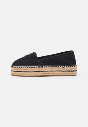 Black canvas espadrille with stitched jute sole, rounded toe, and decorative metal accent on the front. Simple and low-profile design.