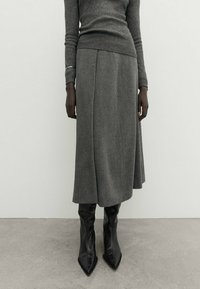 Grå ullblandning midi kjol med rak skärning och subtila veck, kombinerad med eleganta svarta spetsiga ankelskor. Strukturerad stickad tröja.