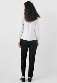 Camicia bianca a maniche lunghe con design aderente, abbinata a pantaloni neri sartoriali e scarpe nere. Estetica semplice e elegante.