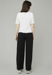 Haut blanc texturé à manches courtes avec une ouverture en forme de clé au dos, associé à un pantalon noir fluide et des baskets de couleur claire. Design simple et moderne.