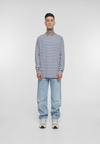 Langermet stripete skjorte i blå og hvit, kombinert med lyseblå slitte jeans og flerfargede sneakers.