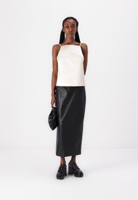 Cream sleeveless top paired with a long black leather skirt. Accessories include a black handbag and chunky black platform shoes.
