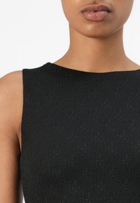 Zwart mouwloos jurk met een textuurstof met een subtiel patroon. De halslijn is rond en het materiaal lijkt licht en soepel.