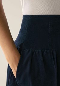 Fustă din catifea cu câneluri de culoare albastru marin, cu tiv evazat și buzunar lateral, văzută din talie până la tiv.