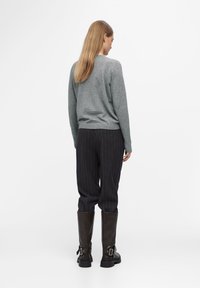Grijze gebreide trui gecombineerd met donkere pinstripe broek en kniehoge bruine leren laarzen, met een matte afwerking en een gespdetail.