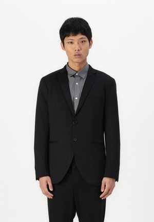 Blazer nero con due bottoni, revers a taglio, e tasche frontali, abbinato a una camicia grigia con colletto. Texture liscia, design strutturato.