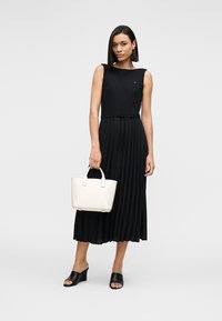 Μαύρο, ριμπ φόρεμα χωρίς μανίκια με πλισέ φούστα και ζώνη με κορδόνι στη μέση. Συνδυάζεται με λευκή τσάντα χειρός και μαύρα σανδάλια με λουράκι.