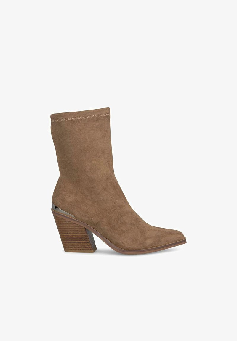 Botină maro din suede, cu vârful ascuțit și toc pe straturi, având un accent metalic pe lateral și detalii subtile de cusătură.