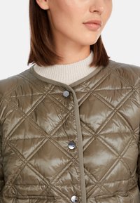 Quilted olivgrüne Jacke mit glänzendem Finish, runden Ausschnitt, cremefarbener Strickkragen und silbernen Druckknöpfen.