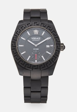 Reloj automático Versace con pulsera y caja de metal negro. Presenta un dial redondo, marcadores de horas plateados y un distintivo patrón de clave griega.