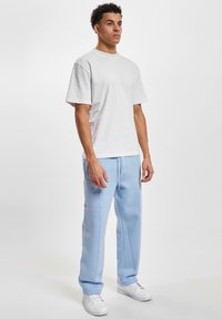 Witte katoenen t-shirt met korte mouwen gecombineerd met lichtblauwe sweatpants. Witte sneakers maken de outfit compleet. Eenvoudig en casual ontwerp.